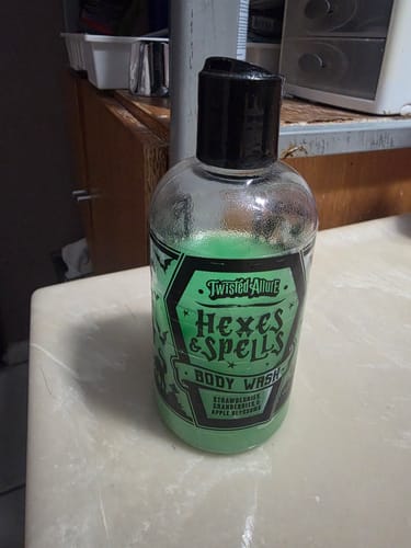 Customer's bottle of Hexes and Spells Body Wash with its bright green liquid, placed on a bathroom counter.