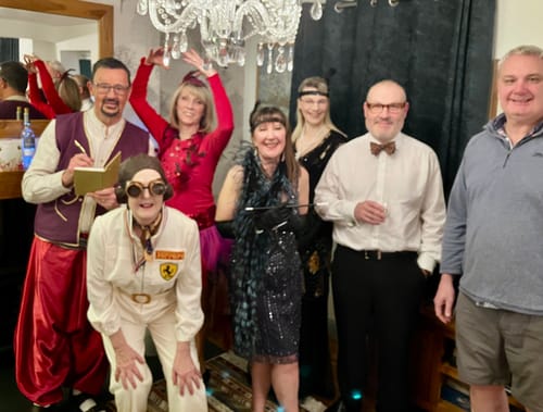 Customers enjoying the Midnight on the Orient Express game in various fun 1920s costumes, posing together under a chandelier.