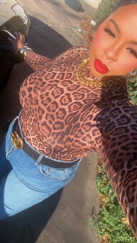 Customer outdoors wearing the long-sleeved Naked Print Bodysuit, styled with blue jeans and a belt.