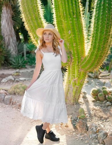 Reviewer wearing black Soft Step shoes with a long white dress and hat in a sunny garden.