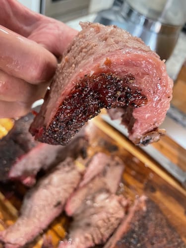 Close-up of a customer holding a thick, juicy slice of smoked USDA Prime Brisket.
