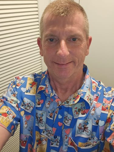 Customer wearing the blue 'Picture Perfect' shirt featuring a colorful collage of Gonzo and Camilla snapshots.