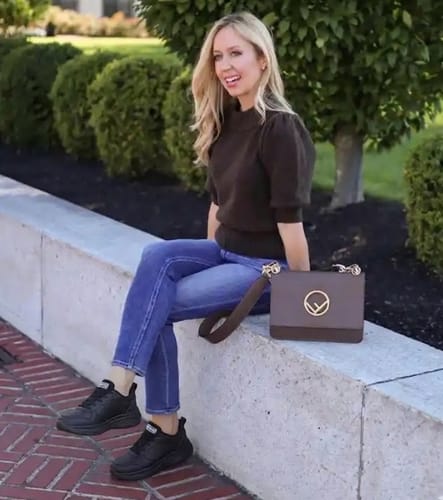 A reviewer sits outdoors styling the black Soft Step shoes with jeans and a puff-sleeve top.