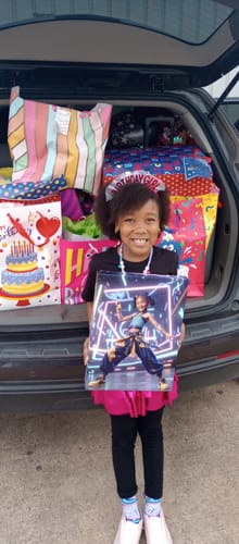 Reviewer's happy child holding her custom portrait, standing by a car filled with birthday gifts.