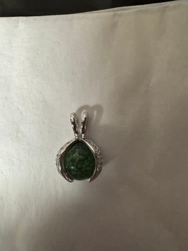 Customer's silver wishbone pendant holding a dark green cremation ash marble on a white surface.