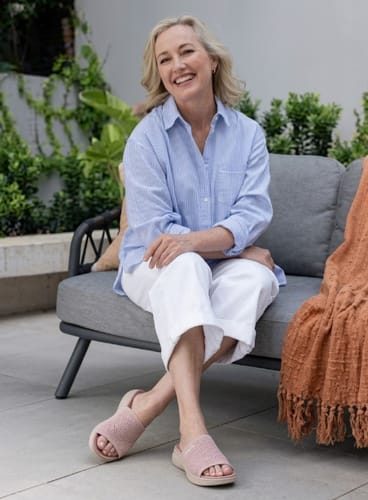 Reviewer sitting on a patio couch wearing the pink Ease slides.