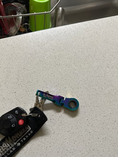 Reviewer's iridescent 10mm Wrench Keychain attached to a set of keys on a countertop.