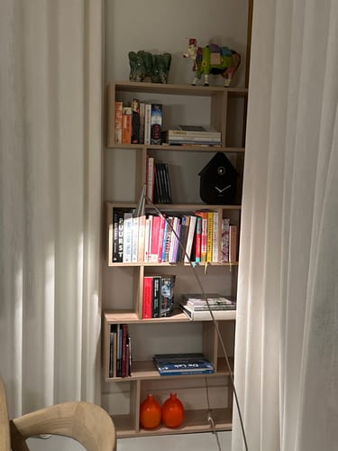 Klant toont de ATHENA boekenkast met eikenlook, gevuld met boeken en decoratie in een kamer.