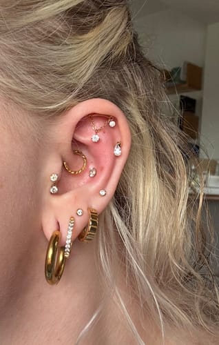 Kundenfoto des Mirelle Hidden Helix Piercings, getragen in einem Ohr mit anderem Goldschmuck.