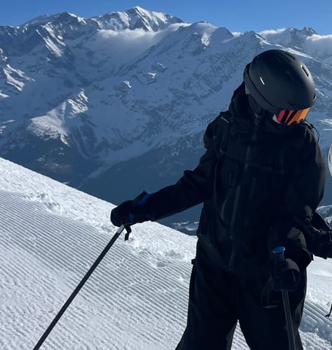 Reviewer wearing the black insulated snow jacket on a ski slope with mountains in the background.