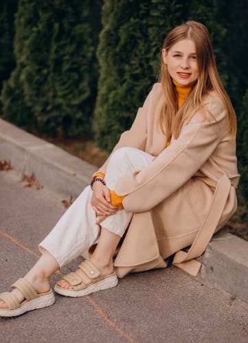 Reviewer sitting outdoors wearing their comfortable beige Relief sandals with white soles.