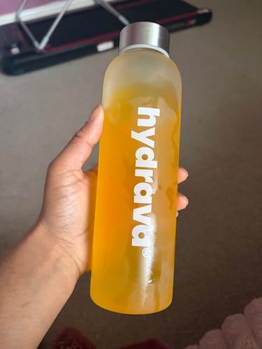 Customer holding a frosted hydrava bottle filled with the orange-colored electrolyte salts drink.