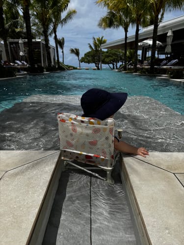 Reviewer's baby sitting in the Clementine baby chair in a shallow pool, seen from the back.
