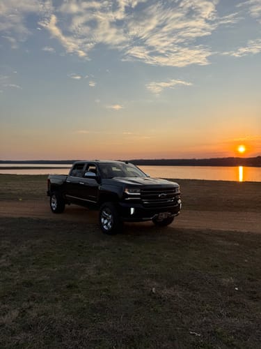 Customer's lifted black Silverado 1500 with the suspension kit installed, parked by a lake at sunset.