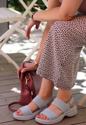 Reviewer wearing light blue Steady sandals with thick soles while sitting outdoors.