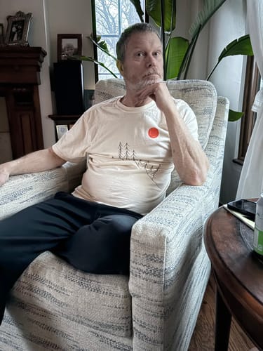 Reviewer sitting in a chair wearing the light-colored Sunrise Pines T-shirt.