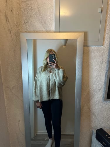 Kundin macht ein Spiegelselfie und trägt den übergroßen Cardigan 'CozyGlam' zu schwarzen Leggings.