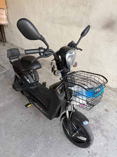 Un cliente muestra su bicicleta eléctrica negra Kiwo ensamblada desde una vista frontal, con la canasta y los espejos visibles.