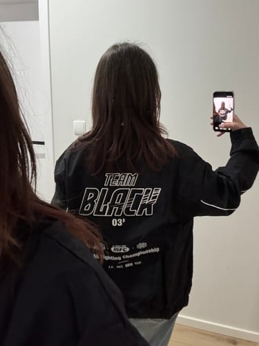 Reviewer takes a mirror selfie wearing the Jinx Team Black Windbreaker, showing the back graphics.