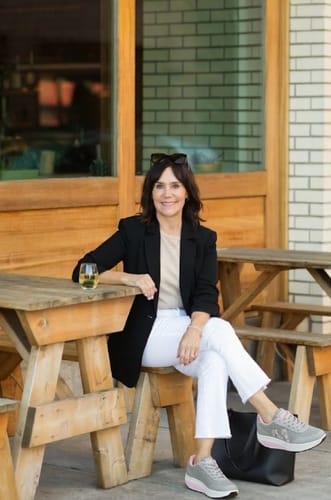 Reviewer sitting at an outdoor table, styling their grey Cloud Lift shoes with white pants and a black blazer.