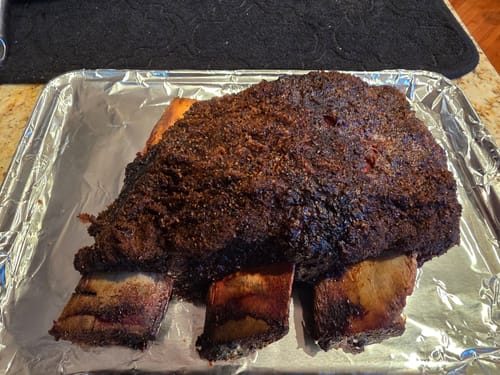 Customer's cooked Bone-In Short Ribs with a dark, seasoned crust, resting on a foil-lined tray.