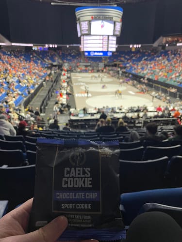 Customer holding a package of Cael's Cookie Chocolate Chip while watching a wrestling match in a large arena.
