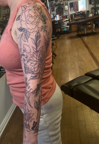 Customer's arm showing the fresh linework of a full floral tattoo sleeve after using the Painless All-Stars Kit.