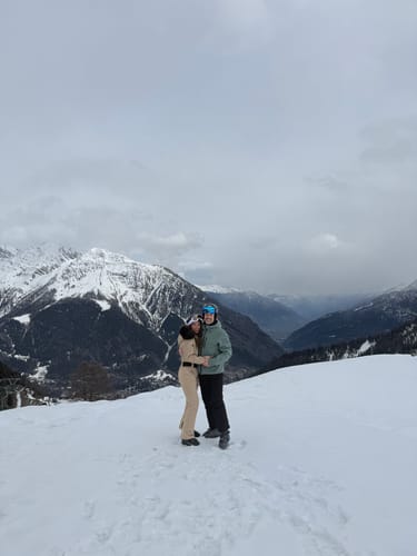 Customer wearing the khaki shirred one-piece ski suit on a snowy mountain.