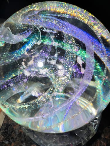 Close-up of reviewer's Dichroic Rainbow Orb showing shimmering spirals of ash and colorful glass inside.