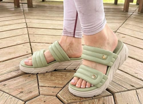 Reviewer wearing the padded, light green Relief sandals while standing on a wooden deck.