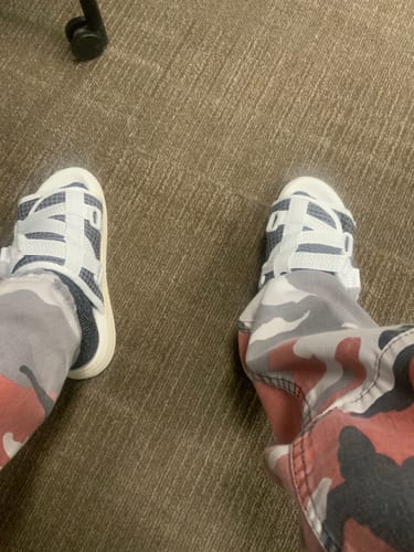 Reviewer's feet, viewed from above, wearing white and blue strappy slides with camouflage pants on a carpeted floor.