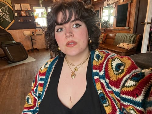 Customer wearing a colorful cardigan and several layered gold necklaces and hoop earrings from the sale.