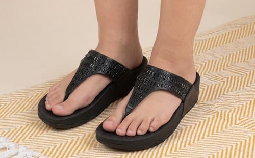 Reviewer's feet in the black Drift sandals, showing the embellished strap and supportive sole on a patterned rug.