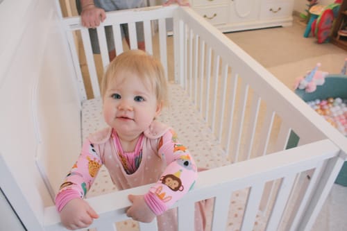 Customer's baby wearing the Rose 4 Season Ultimate Baby Sleep Bag while standing in a white crib.
