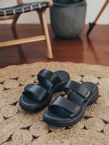 Customer's black Balance sandals with two adjustable straps, shown resting on a woven jute rug.