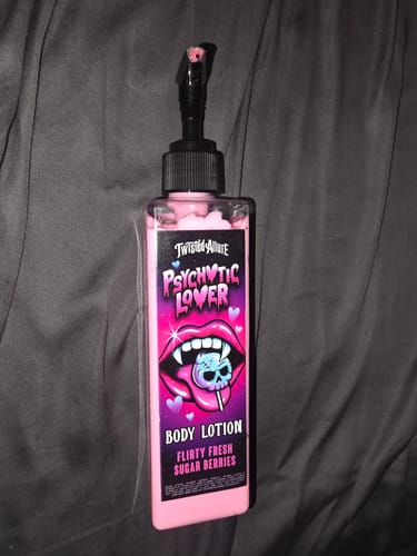Reviewer's bottle of pink Psychotic Lover Body Lotion with a black pump, set against a gray fabric background.