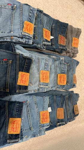Customer's bale of plus-size jeans in various blue washes, folded and laid out in rows on the floor.