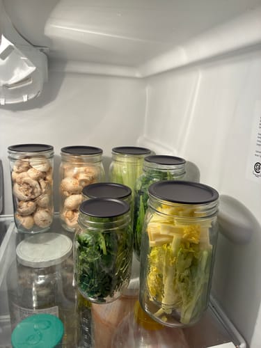 Customer's fresh mushrooms and greens in mason jars, sealed with the Mason Genie® Vacuum Sealer Kit, organized in a refrigerator.