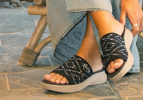 A reviewer wearing the Ease sandals, showing the woven black strap and thick cushioned sole.