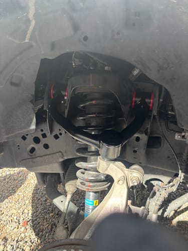 Customer's new black Upper Control Arm with red bushings installed on a truck's front suspension.
