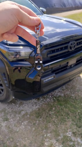 Customer holding a black 10mm Wrench Keychain in front of a truck.