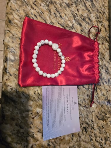 Reviewer's Howlite crystal bracelet from their monthly box, shown on its red bag with an information card.