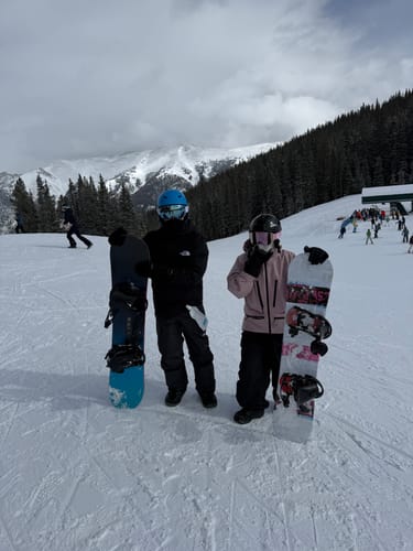 Reviewer wearing the pink snow jacket, showing its oversized fit while standing on a snowy slope with another person.