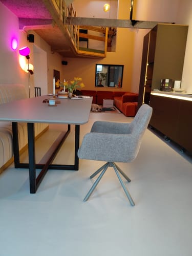 Klant toont de taupe by fonQ Weld eetkamerstoel aan een lichte eettafel in een modern interieur.