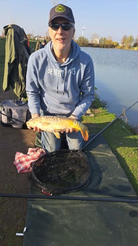 Klant knielt aan de waterkant en houdt een mooie karper omhoog, gevangen met SUPERCRUSH 2kg.