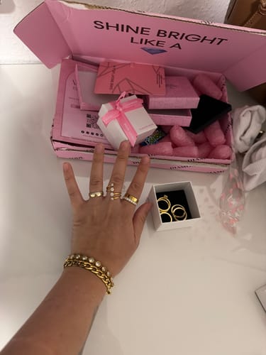 Hand eines Kunden, die den goldenen Glow Lines Ring zusammen mit anderem Schmuck trägt.