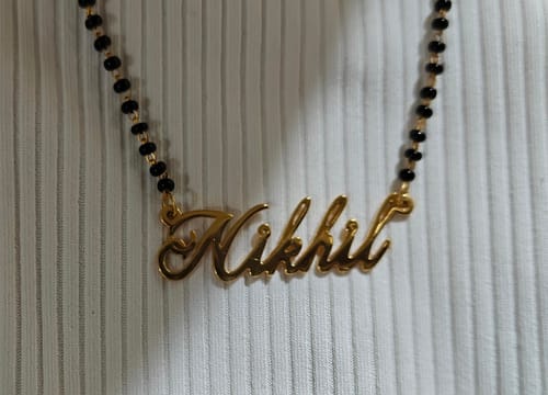 Customer's golden personalised mangalsutra with the name 'Nikhil' on the pendant, shown on its black beaded chain.