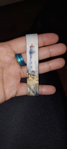 Customer's hand holding the You Guide Me Still Bracelet, showing the detailed lighthouse illustration.