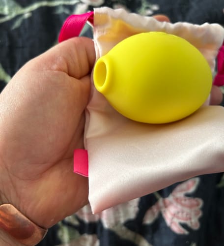 Customer holding the bright yellow Lem Clitoral Massager, resting in its satin pouch.