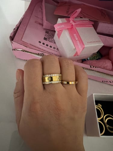Kundenhand trägt den schmalen, vergoldeten Arianna Ring mit Zirkonia-Steinen neben einem anderen goldenen Ring.